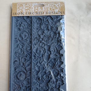 May include: A blue silicone mould from Iron Orchid Designs, featuring detailed floral and scrollwork patterns. The mould is packaged in a clear plastic sleeve with a brown paper header. The text "Iron Orchid Designs" and "Trimmings 4" are visible.