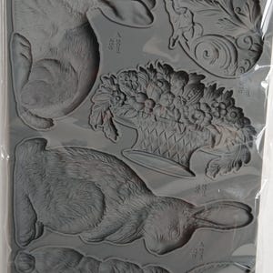 Könnte beinhalten: Eine graue Silikonform mit verschiedenen Designs, darunter Hasen, Blumenarrangements und eine klassische Figur. Die Form ist mit "IRON ORCHID DESIGNS MOULD" und "LES LAPINS" beschriftet. Maße sind in Millilitern und Gramm angegeben.