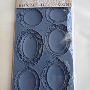 May include: A grey silicone mould by Iron Orchid Designs, featuring six oval vintage brooch designs. The mould includes detailed floral and ornate frame patterns. The packaging reads "VINTAGE BROOCHES". Measurements are in millilitres.