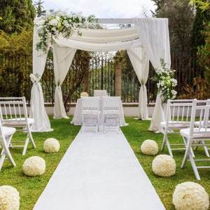 May include: White wedding ceremony setup with white chairs, a white aisle runner, and a white canopy decorated with white flowers.