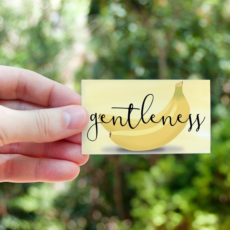 K&ouml;nnte beinhalten: Eine gelbe Karte mit einer gelben Bananenillustration und dem Wort "gentleness" in schwarzer Kursivschrift.