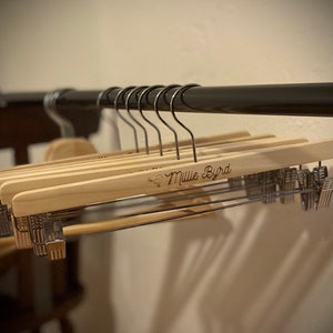 May include: A set of wooden hangers with a metal clip on each end. The hangers are engraved with the text "Millie Byrd".
