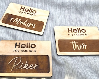May include: Three wooden name tags with the text "Hello my name is" and a name in cursive. The names are Madison, Riker, and Theo.