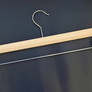 May include: A wooden clothes hanger with a metal hook and two metal clips. The hanger is light brown and the clips are silver.
