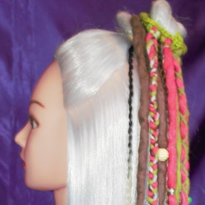 May include: A white wig with long, straight hair. The wig has several colorful braids with beads and charms attached. The braids are in shades of brown, pink, green, and white.