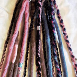 Könnte beinhalten: Ein Set aus bunten synthetischen Dreadlocks mit silbernen Perlen. Die Dreadlocks sind in den Farben Rosa, Braun, Schwarz und Blau.