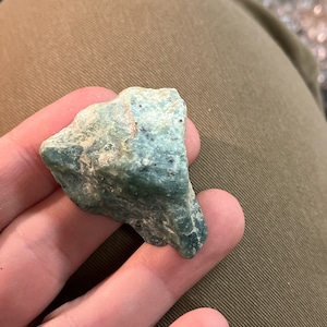 May include: A rough, green, and gray rock with a jagged edge. The rock has a speckled appearance.