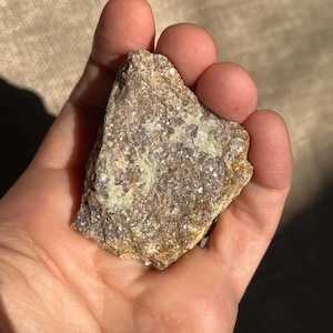 May include: A rough, gray and purple lepidolite crystal with a sparkly, glittery texture.