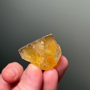 May include: A yellow calcite crystal with a rough, natural texture. The crystal is translucent and has a slight orange hue.