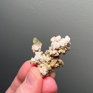 May include: A small cluster of light yellow crystals on a white and brown rock matrix.
