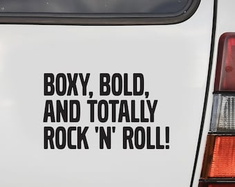 May include: White Volvo 240 GL station wagon with a black bumper and a license plate that reads "359". A black sticker on the back reads "Boxy, Bold, and Totally Rock 'n' Roll!"