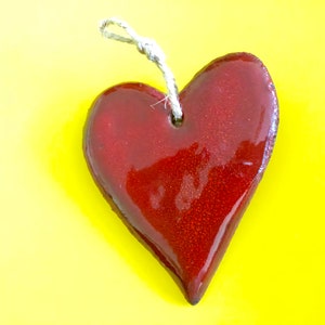 May include: A red heart-shaped ceramic ornament with a string loop for hanging. The ornament is glossy and has a speckled texture.