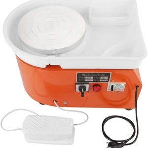 Op de afbeelding: Een oranje en wit pottenbakkerswiel met een witte draaischijf, een wit bassin en een voetpedaal. Het wiel heeft een bedieningspaneel met schakelaars en een netsnoer. Het voetpedaal is met een witte kabel met het wiel verbonden.