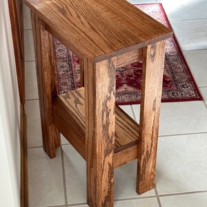 May include: A tall, narrow wooden side table with a rectangular top and a lower shelf. The table features a medium-brown wood grain finish and is constructed with four straight, sturdy legs that support both the top surface and the shelf.