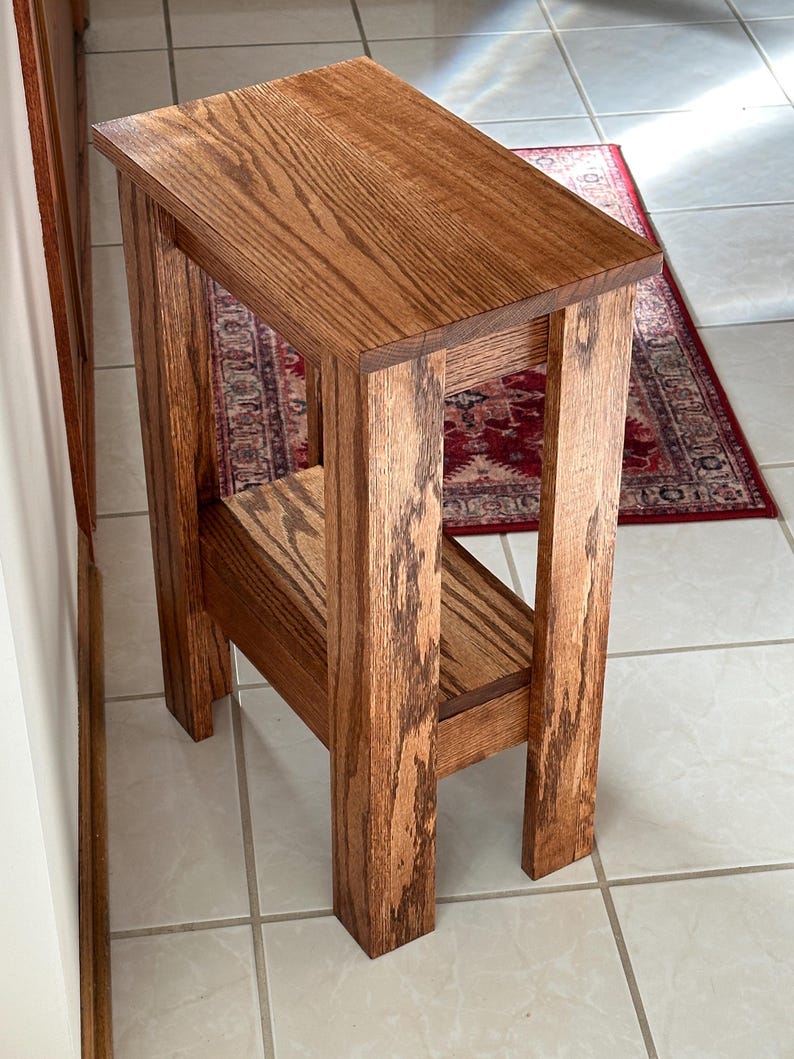 May include: A tall, narrow wooden side table with a rectangular top and a lower shelf. The table features a medium-brown wood grain finish and is constructed with four straight, sturdy legs that support both the top surface and the shelf.