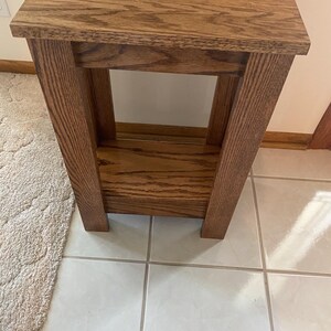 May include: A rectangular wooden side table with a medium brown finish and visible wood grain. The table features a flat top surface, four sturdy vertical legs, and a lower shelf positioned between the legs, providing an open storage area.