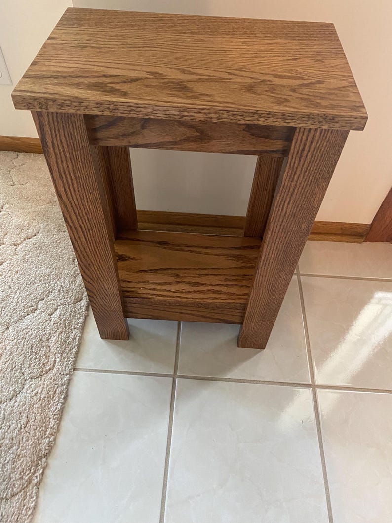 May include: A rectangular wooden side table with a medium brown finish and visible wood grain. The table features a flat top surface, four sturdy vertical legs, and a lower shelf positioned between the legs, providing an open storage area.