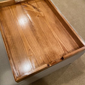 May include: A rectangular wooden tray with a warm brown finish. The tray has a raised edge and a cutout on one side. The wood grain is visible, adding texture to the surface. This tray is suitable for serving or display.