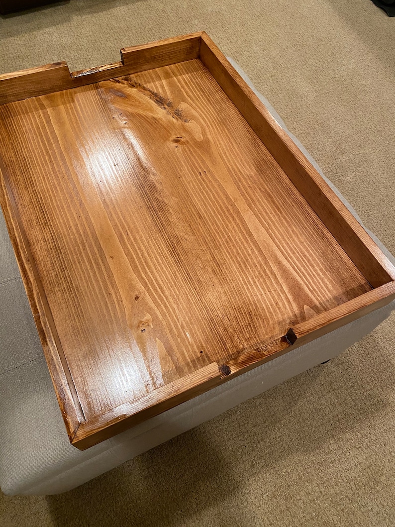 May include: A rectangular wooden tray with a warm brown finish. The tray has a raised edge and a cutout on one side. The wood grain is visible, adding texture to the surface. This tray is suitable for serving or display.