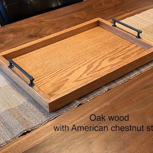May include: A wooden serving tray made of oak wood with an American chestnut stain. The tray has two black metal handles.