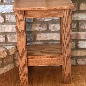 May include: A rectangular wooden side table with a natural brown wood grain finish. The table features a flat top surface, four straight legs, and a lower shelf positioned between the legs, providing an open storage area beneath the main top.