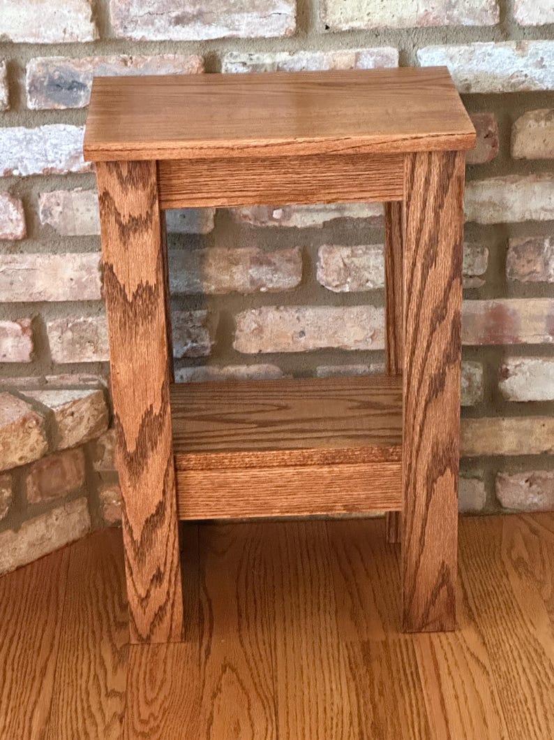 May include: A rectangular wooden side table with a natural brown wood grain finish. The table features a flat top surface, four straight legs, and a lower shelf positioned between the legs, providing an open storage area beneath the main top.