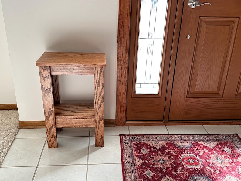 May include: A rectangular wooden side table with a medium brown finish and visible wood grain. The table features a flat top surface, four straight legs, and a lower shelf positioned between the legs, constructed with a simple, open frame design.
