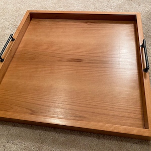 May include: A rectangular wooden serving tray with black metal handles. The tray has a natural wood finish and is made of solid wood.