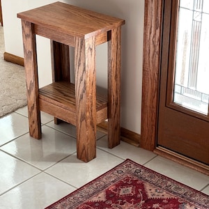 May include: A rectangular wooden side table featuring a medium brown wood grain finish, four sturdy straight legs, and a lower shelf positioned between the legs. The table has a flat top surface and a clean, simple construction design.