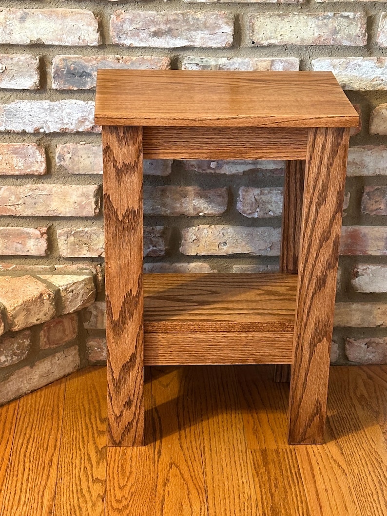May include: A rectangular wooden side table featuring a medium brown finish with a visible wood grain pattern. The table has a flat top surface, four straight legs, and a lower shelf positioned between the legs, constructed from solid wood.