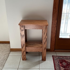 May include: A rectangular wooden side table featuring a medium brown finish with a visible wood grain pattern. The table has four straight legs, a flat top surface, and a lower shelf positioned between the legs, providing an open storage area.