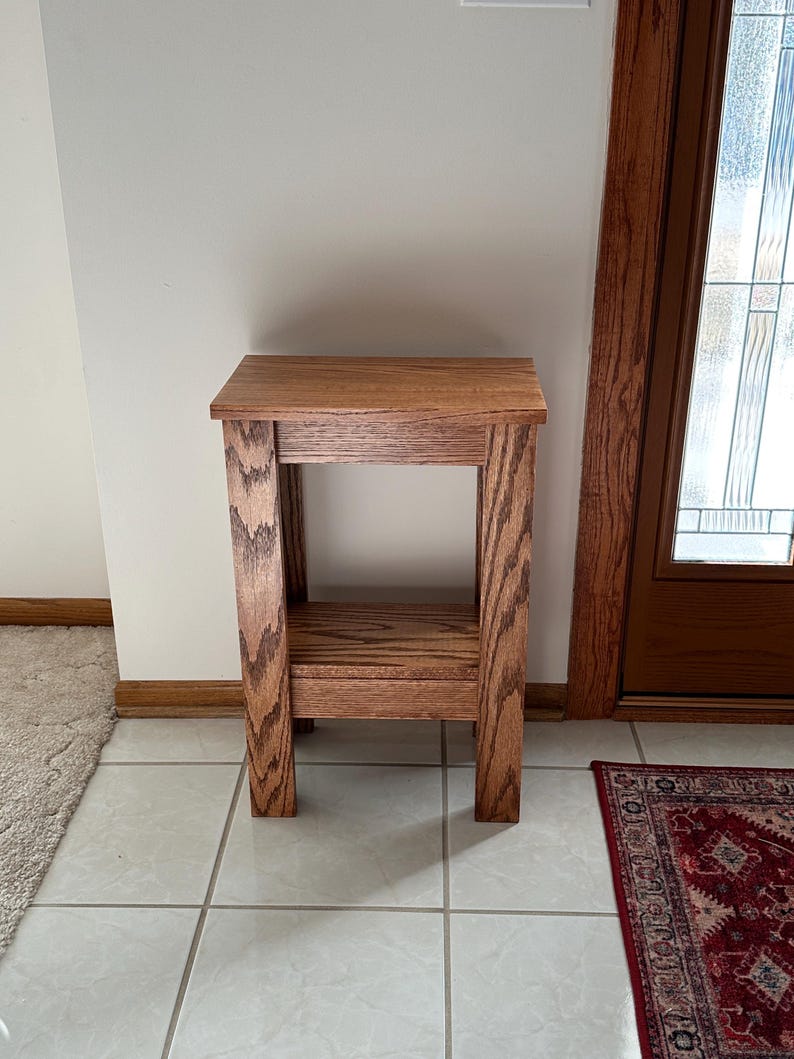 May include: A rectangular wooden side table featuring a medium brown finish with a visible wood grain pattern. The table has four straight legs, a flat top surface, and a lower shelf positioned between the legs, providing an open storage area.