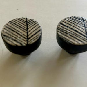 May include: Two black and white ceramic knobs with a geometric pattern. The knobs are round and have a black base.