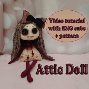Puede incluir: Una muñeca de ático hecha a mano con ojos de botón, boca cosida y pelo largo y rizado de color marrón. La muñeca lleva un lazo negro, un cuello rojo y negro y un vestido estampado. Las piernas de la muñeca están cruzadas y son rojas. El texto de la imagen dice: "Video tutorial with ENG subs + pattern".