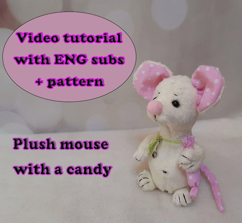 May include: A cream-colored plush mouse with pink polka-dot ears and a matching pink polka-dot candy accessory. The mouse wears a thin green ribbon around its neck with a small silver charm. Text reads: Video tutorial with ENG subs + pattern.