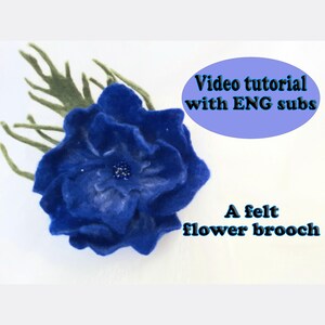 May include: A deep blue felt flower brooch with layered petals and a dark center, accompanied by green felt leaves. Text on the image reads: Video tutorial with ENG subs and A felt flower brooch.