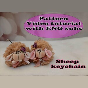 May include: Two plush sheep keychains with curly tan wool, pink fabric ears, and small bows. One sheep has a dark purple flower accent. Text on the image reads: Pattern Video tutorial with ENG subs and Sheep keychain.