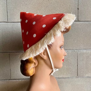 Può includere: Un cappello rosso con pois bianchi e un bordo di frangia bianca. Il cappello ha una corona a punta e un cinturino per il mento.