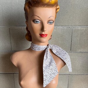 May include: A white scarf with a brown musical note pattern tied around a mannequin's neck.