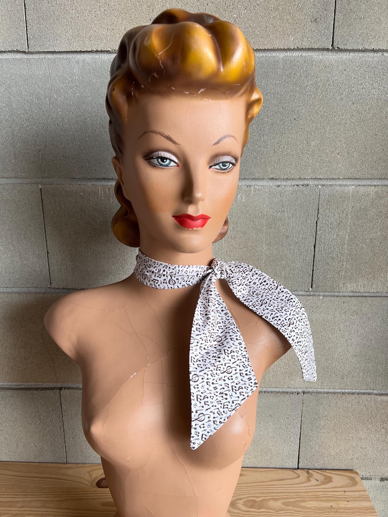 May include: A white scarf with a brown musical note pattern tied around a mannequin's neck.