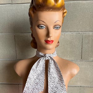 May include: A white necktie with a black musical note pattern. The necktie is tied around a mannequin's neck.