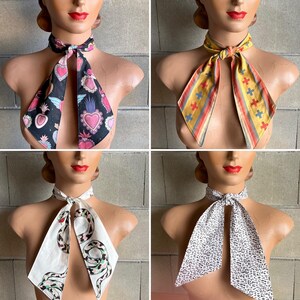 May include: Four different neckties with various patterns. The neckties are tied in a bow and are displayed on mannequins. The patterns include a black and pink heart design, a yellow and red striped design, a white and green snake design, and a black and white abstract design.