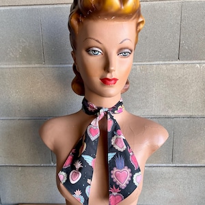 May include: A black necktie with a pattern of pink, blue, and white sacred hearts on a black background. The tie is tied in a bow around a mannequin's neck.