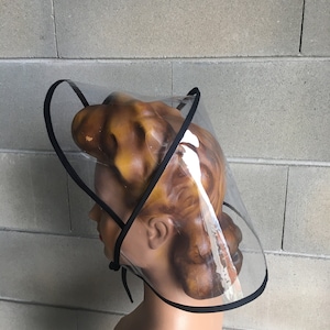 Op de afbeelding: Een transparant plastic vizier met een zwarte rand. Het vizier wordt gedragen op een mannequinhoofd.