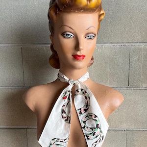 May include: A white silk scarf with a green and pink snake print. The scarf is tied around the neck of a mannequin.