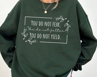 May include: A dark green sweatshirt with the text "YOU DO NOT FEAR. You do not falter. YOU DO NOT YIELD." printed in white.