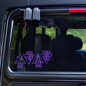 Op de afbeelding: Paarse vinylstickers op een autoraam. De stickers tonen geometrische vormen met de woorden AER, AQUA, IGNIS en TERRA, die elk een element vertegenwoordigen. Het ontwerp is een gestileerde weergave van de elementen.