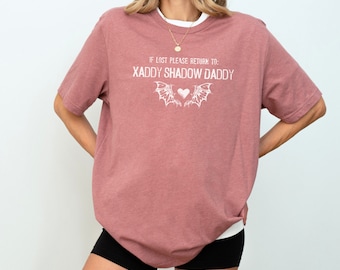Puede incluir: Una camiseta de gran tamaño de color rosa polvoriento con el texto "IF LOST PLEASE RETURN TO: XADDY SHADOW DADDY" y un corazón blanco con alas.