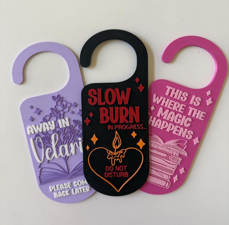 May include: Three decorative door hangers in purple, black, and pink. The purple hanger has floral and text details. The black hanger says "Slow Burn" and "Do Not Disturb". The pink hanger says "This is Where the Magic Happens".