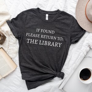 May include: A dark gray t-shirt with the text "IF FOUND PLEASE RETURN TO: THE LIBRARY" printed in white.